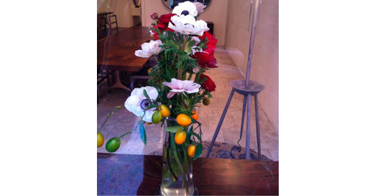 White and red flowers with orange and green fruits in a vase.