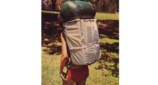 Back view of a woman carrying large back pack and sleeping bag.