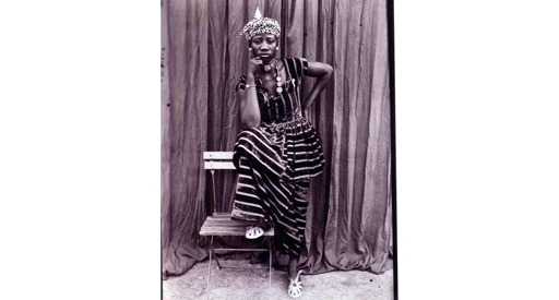 Black and white photo of a woman in a striped dress with one foot on a chair.