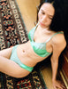 A model posing on the floor while wearing the Willow Bralette in the color Sage and the Saffi Panty in Sage.